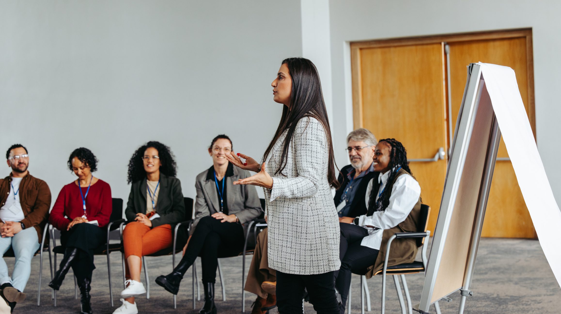 Female instructor leading teambuilding session with diverse group in modern office setting Woman speaking to a seated group.